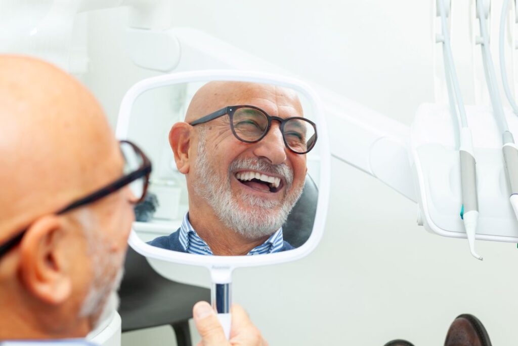 A man smiling in the mirror at his dental implants